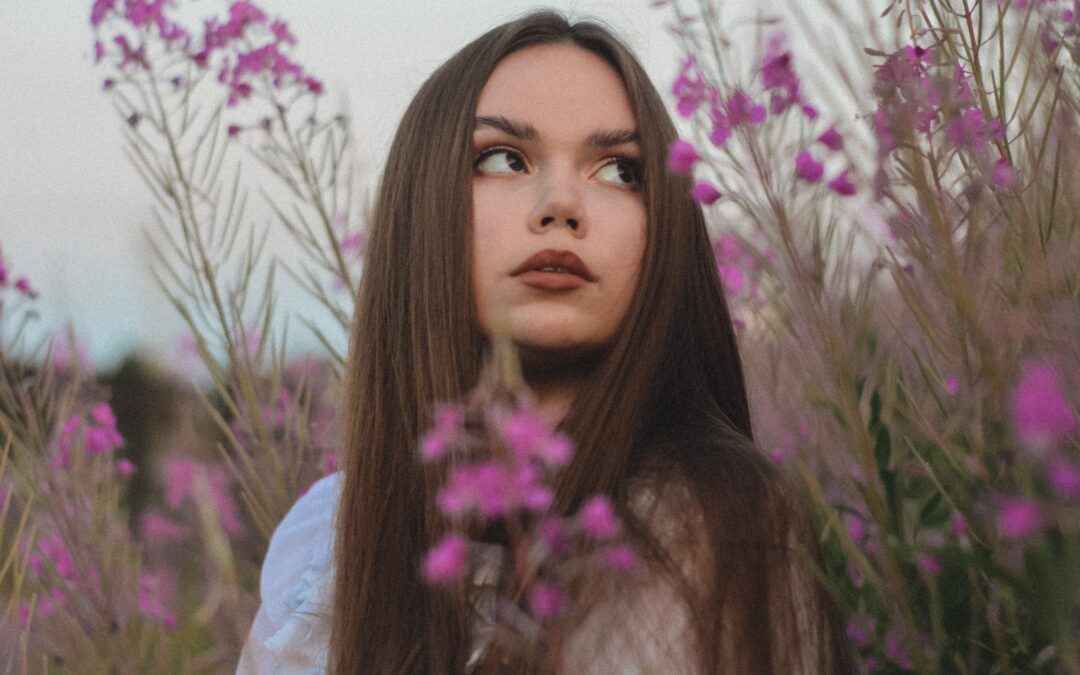 A brunette in a field of flowers with long, smooth hair from a Brazilian Blowout.